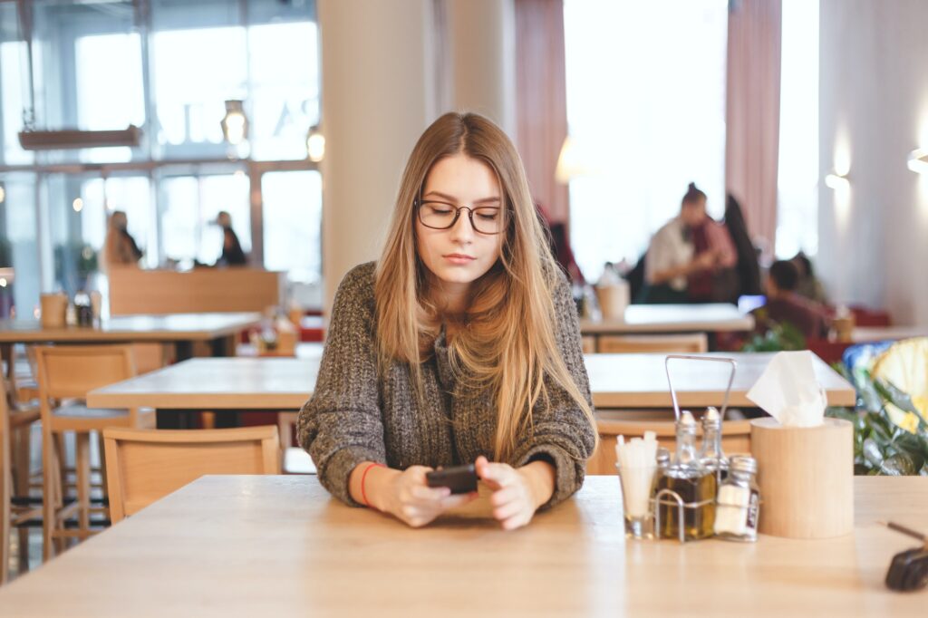 Portrait of cute freelancer girl sitting in a cafe. She wears brown hipster eyeglasses.